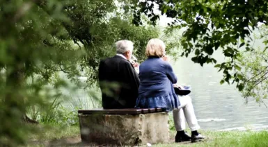 two people sitting on pavement facing on body of water
