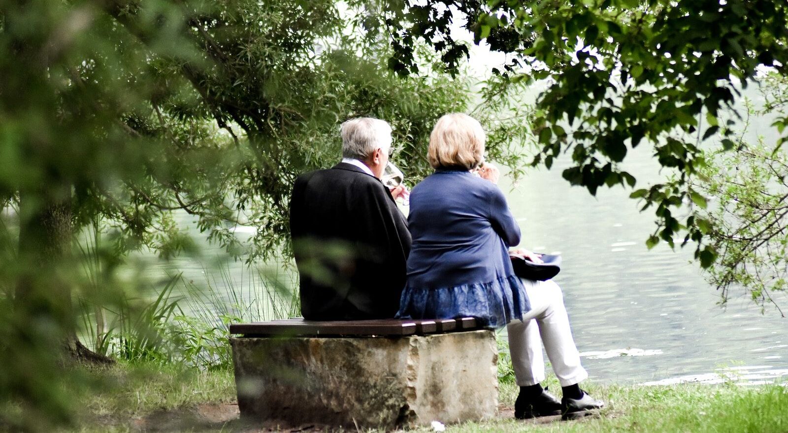 two people sitting on pavement facing on body of water