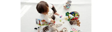 boy sitting on white cloth surrounded by toys