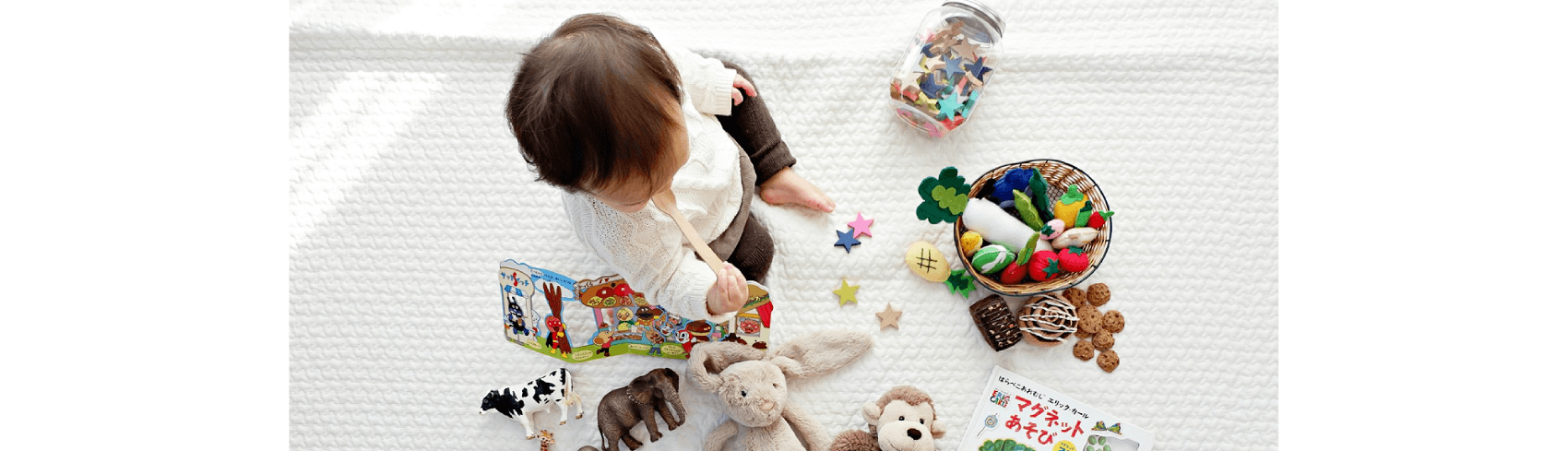 boy sitting on white cloth surrounded by toys